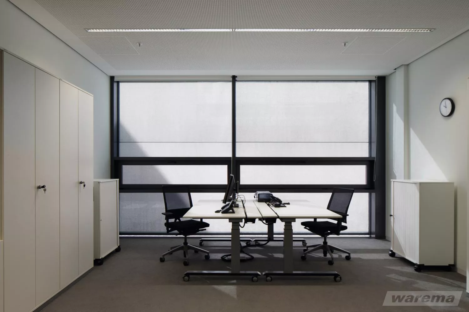 Aufnahme eines Büroraums mit Blick richtung Fenster mit heruntergelassenem Sonnenschutz.